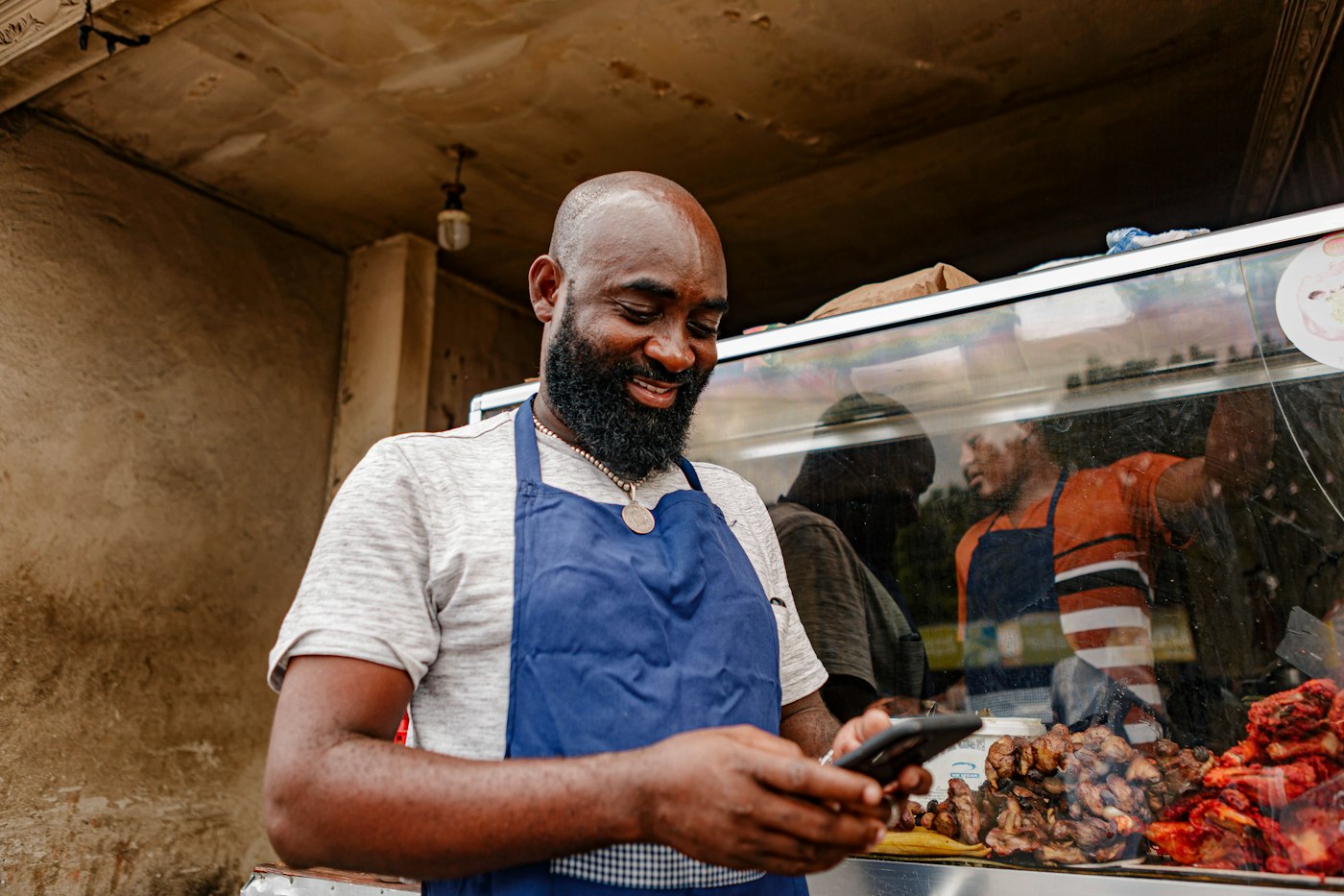 Café owner in an apron checking sales on his phone behind the counter
