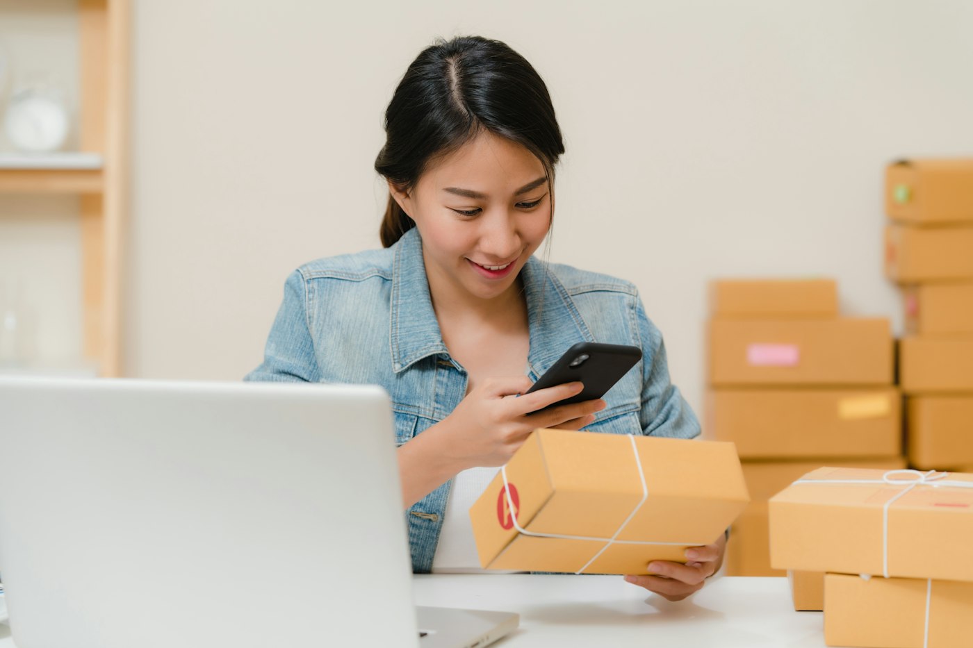Online shop owner checking an order on her phone beside packed boxes